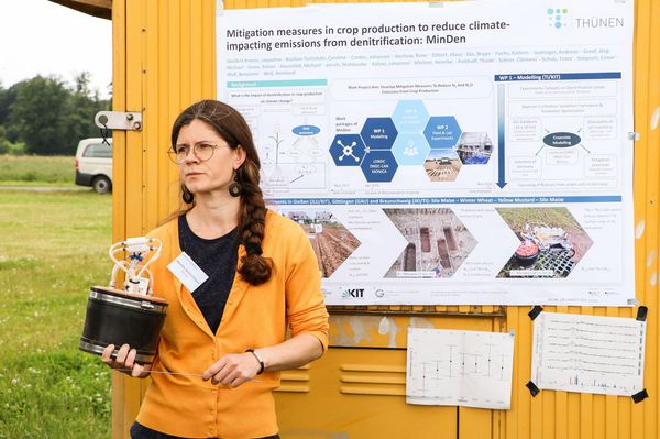 Eine Wissenschaftlerin hält ein Gerät in der Hand und steht vor einem Poster